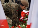 Osoba w mundurze składa kwiaty przed pomnikiem