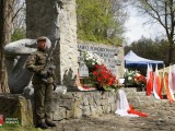 Żołnierz, kwiaty i flagi przed pomnikiem