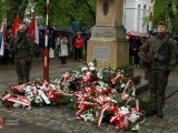 Żołnierze i kwiaty przy pomniku, w tle grupa osób