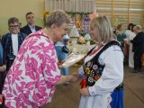 Przedstawicielka władz wręcza dyplom kobiecie w stroju ludowym ozdobionym haftami i koralami
